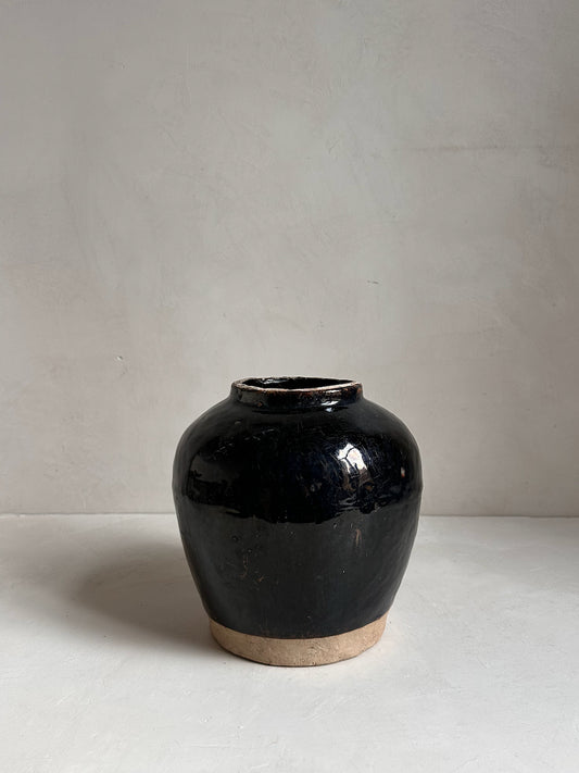 Black ceramic jar on a white surface with a light gray background